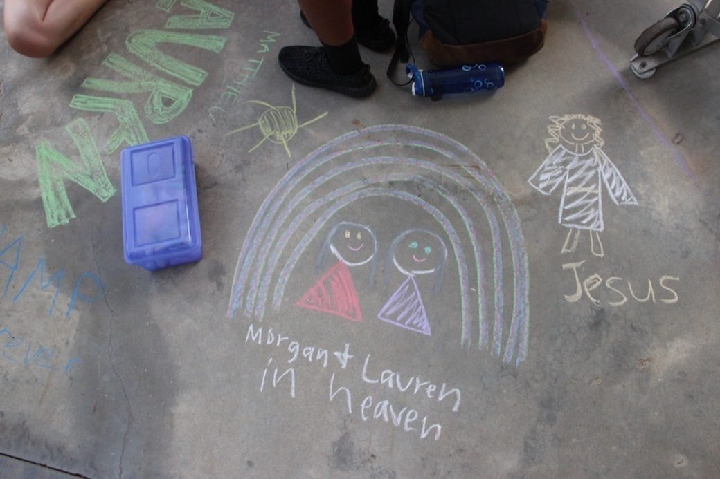 Children's chalk drawing of a rainbow, two friends, and Jesus