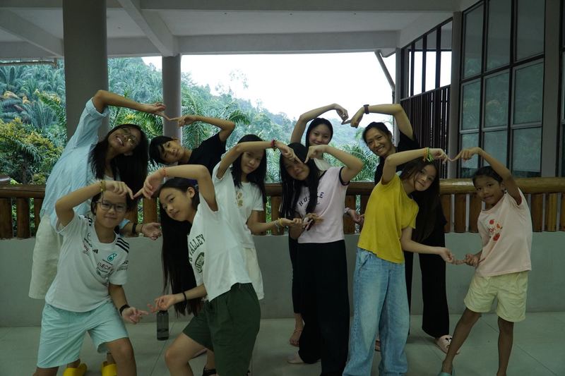 Campers and counselors making heart shapes with their arms on a veranda above the Malaysian jungle